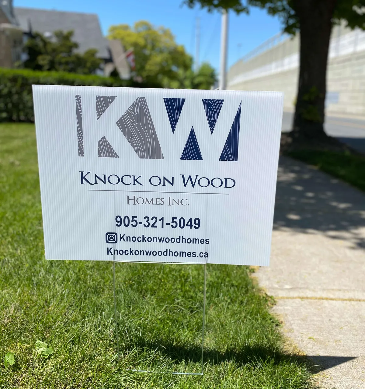 Knock on Wood Homes lawn sign with the KW logo and phone number 905-321-5049, staked on a front lawn at a job site