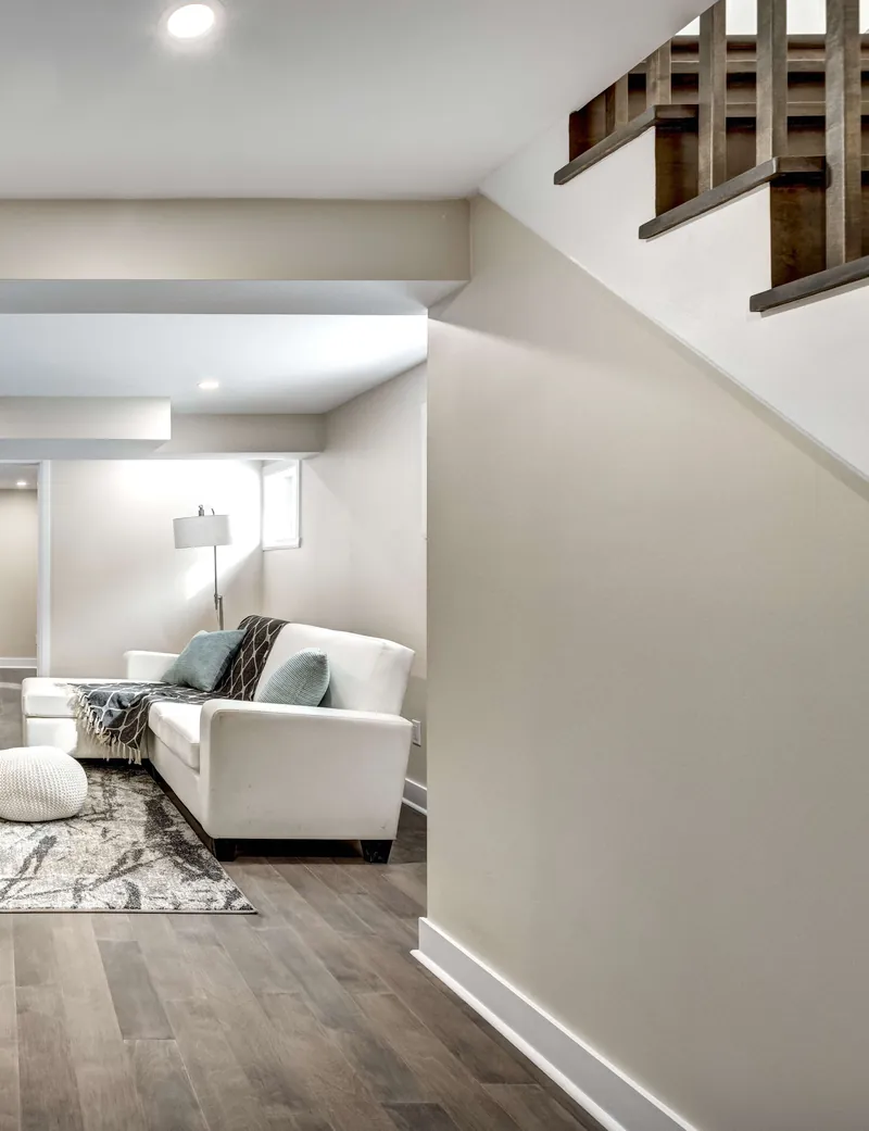 Finished basement lounge with a white sofa beside the new staircase