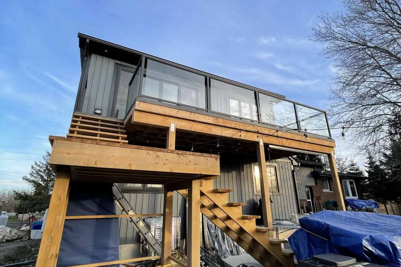 New two-level wood deck with glass railings and a staircase down to the yard