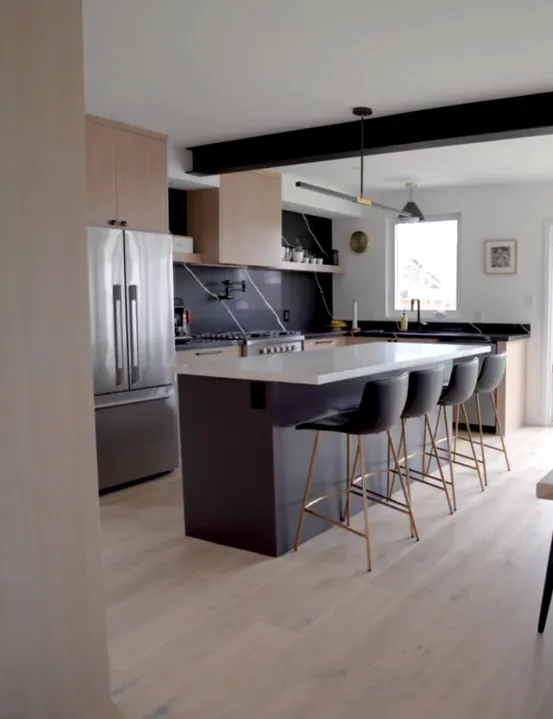 Renovated kitchen with a dark island, bar stools, stainless fridge and a black backsplash