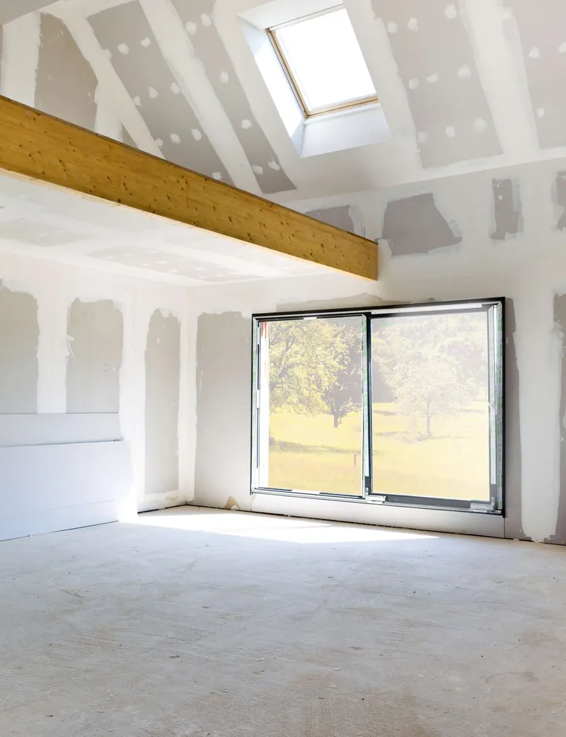 Before: an upper-floor room stripped to drywall and bare subfloor beneath a skylight
